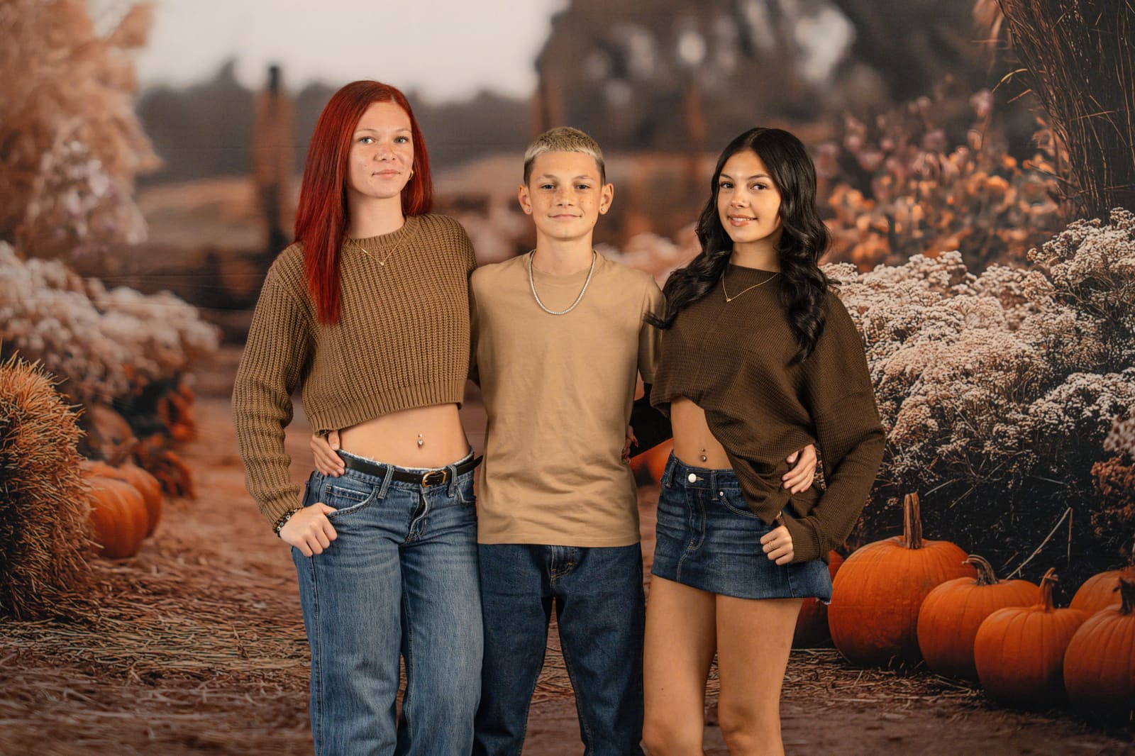 Three teenage siblings standing arm in arm in the harvest field set.