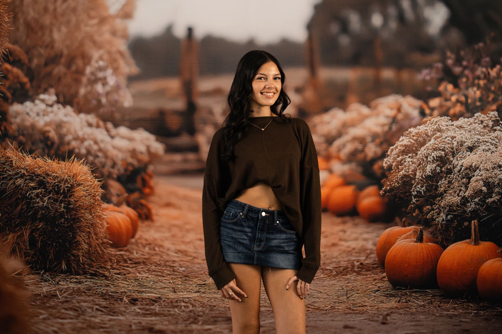 Teenage girl smiling on the harvest field path lined with pumpkins.