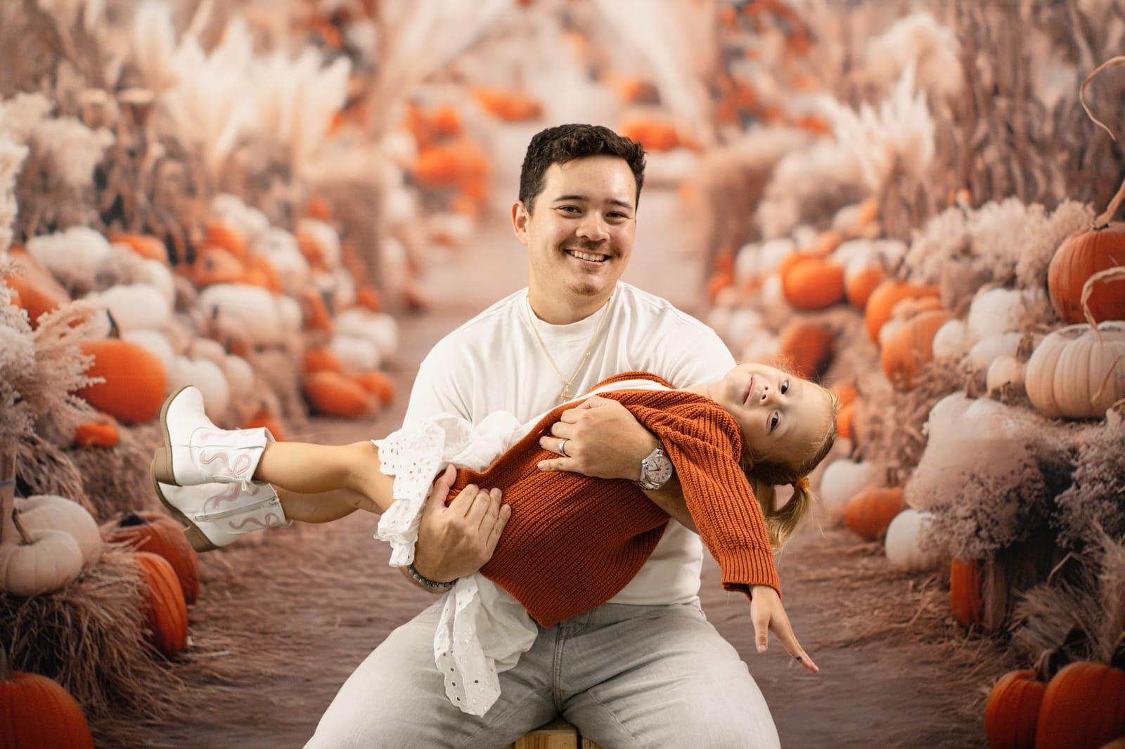 Father playfully cradling his laughing daughter in the pumpkin patch set.