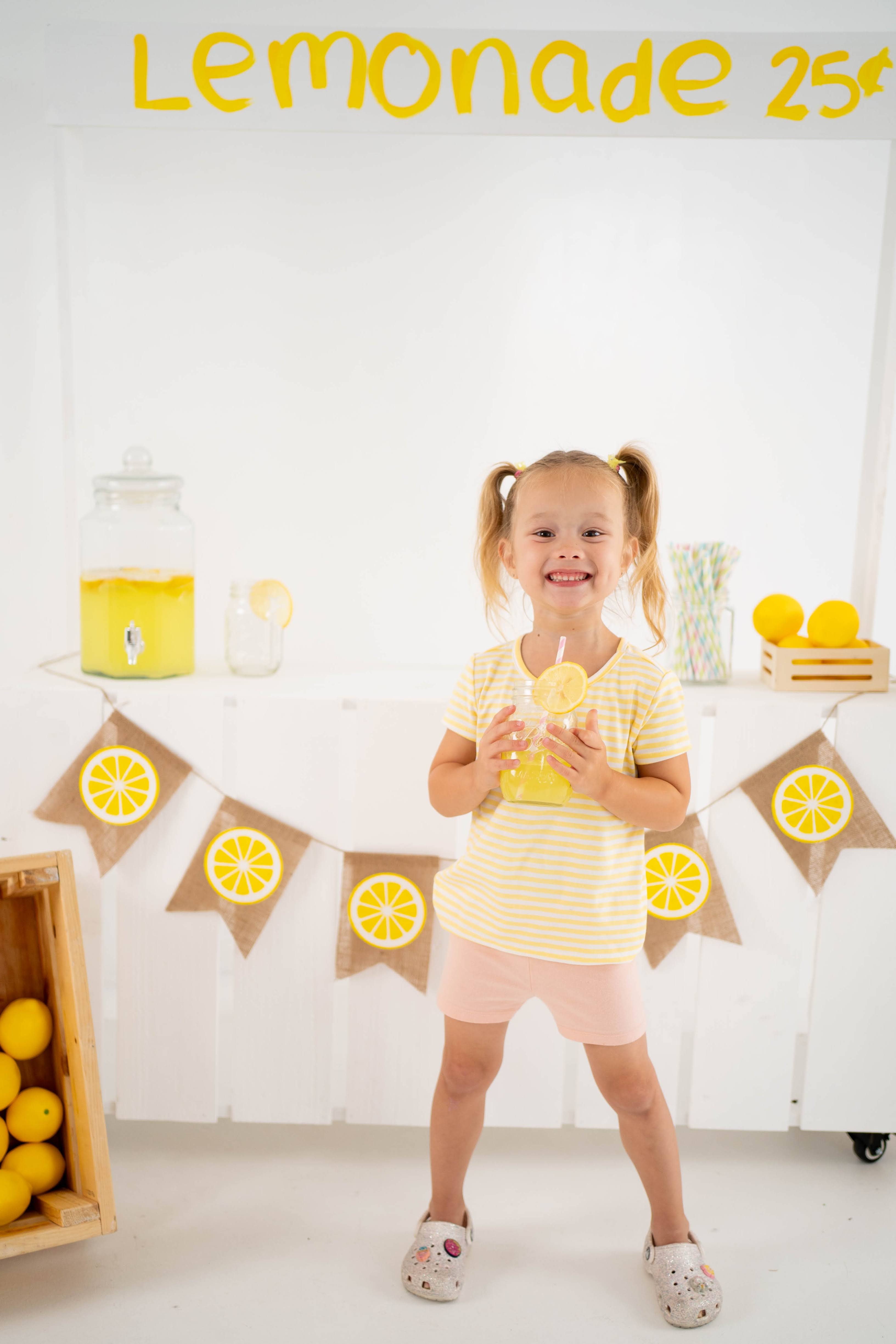 Girl smiling beside the lemonade stand with lemons in the foreground.