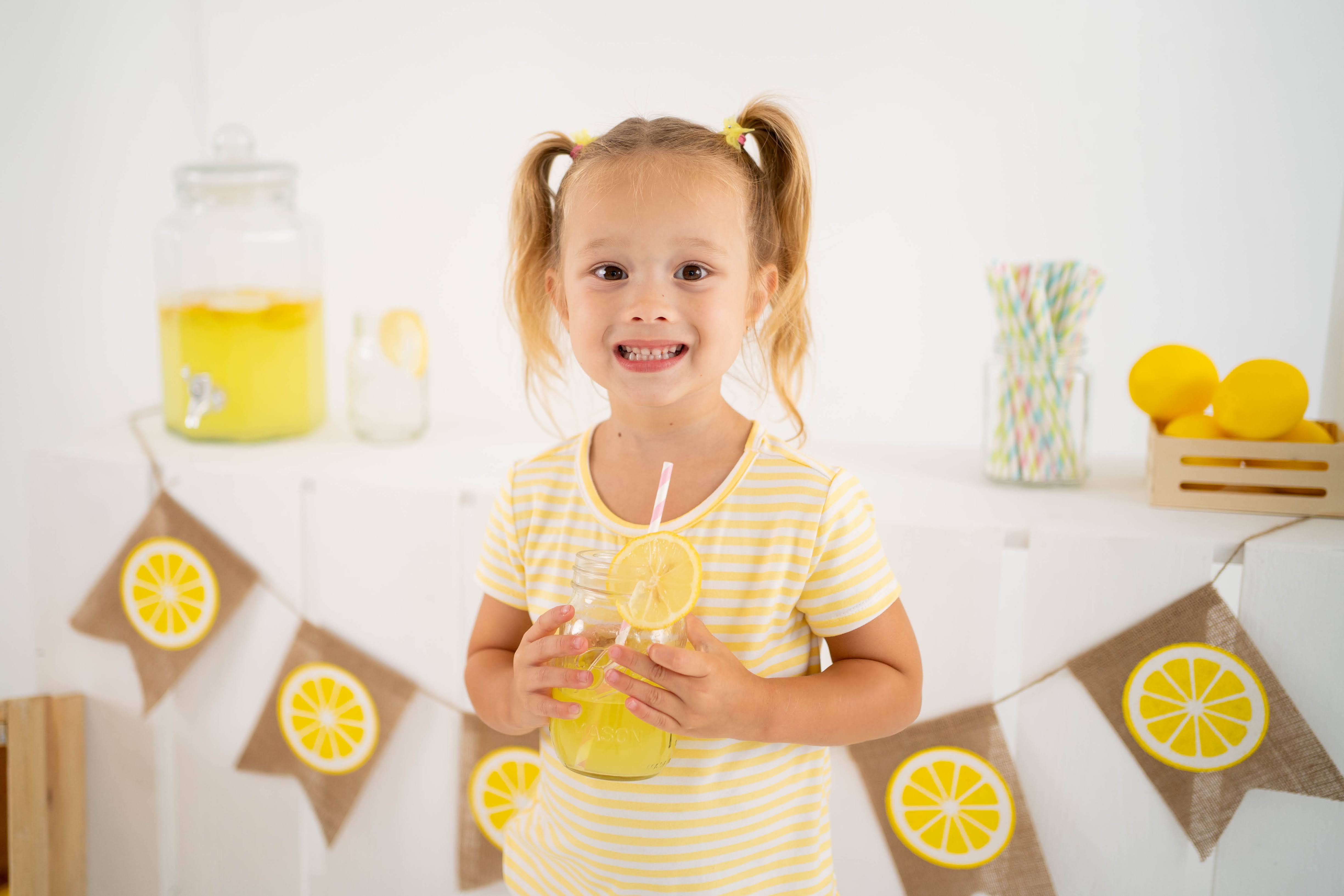 Girl smiling with a lemonade jar in front of lemon slice bunting.